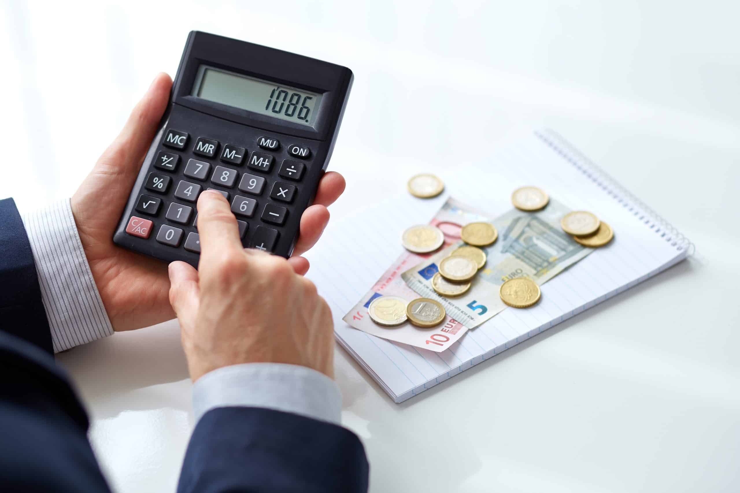 Un hombre sostiene una calculadora y monedas sobre un escritorio.